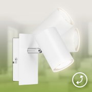 Witte wandlamp met drie afzonderlijk draaibare cilindervormige spots, schuin van voren gezien tegen een onscherpe groene achtergrond