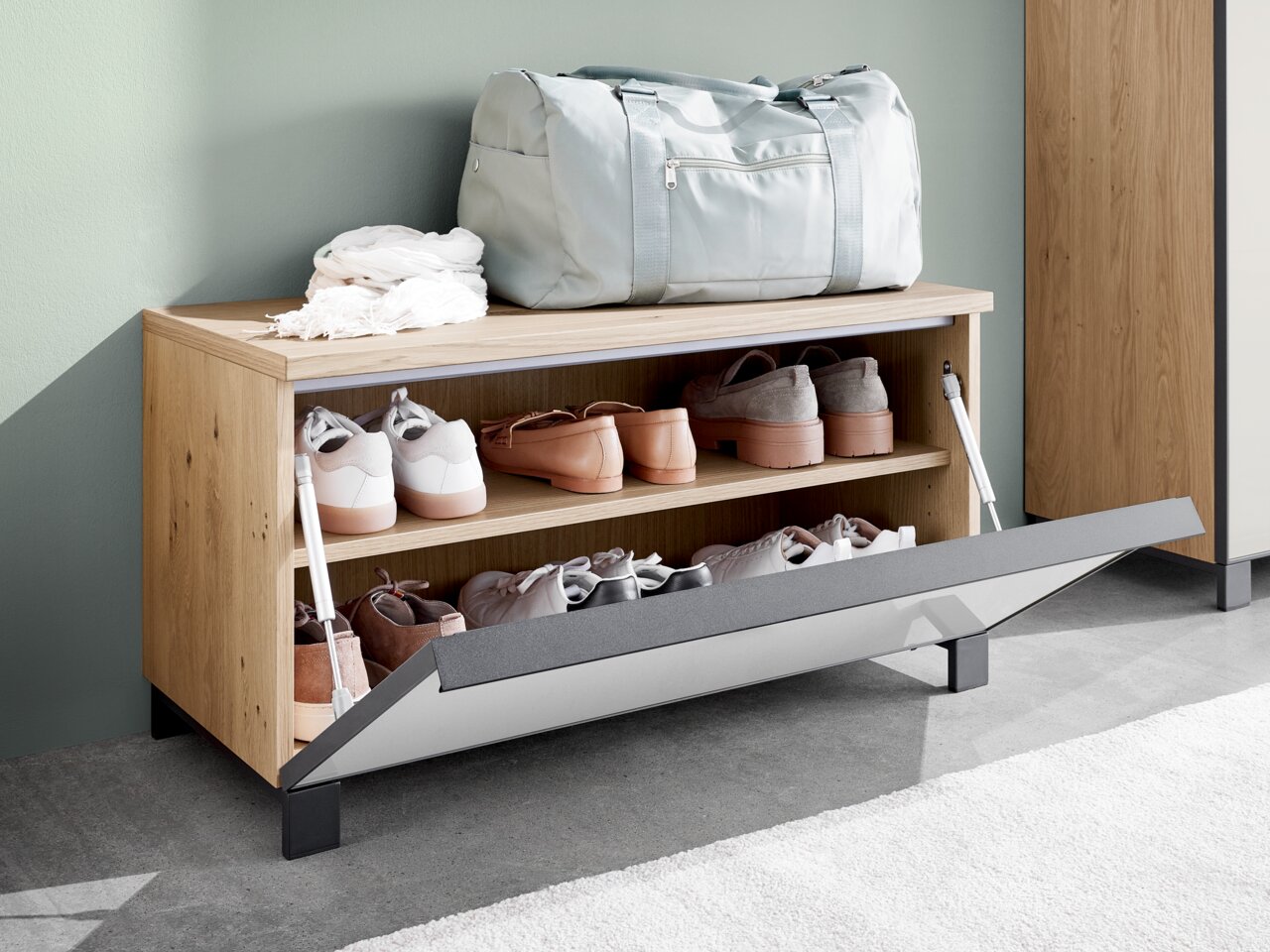 Houten garderobebank met een open klep, waarop schoenen op twee planken te zien zijn, met daarop een tas en een sjaal, zijaanzicht.
