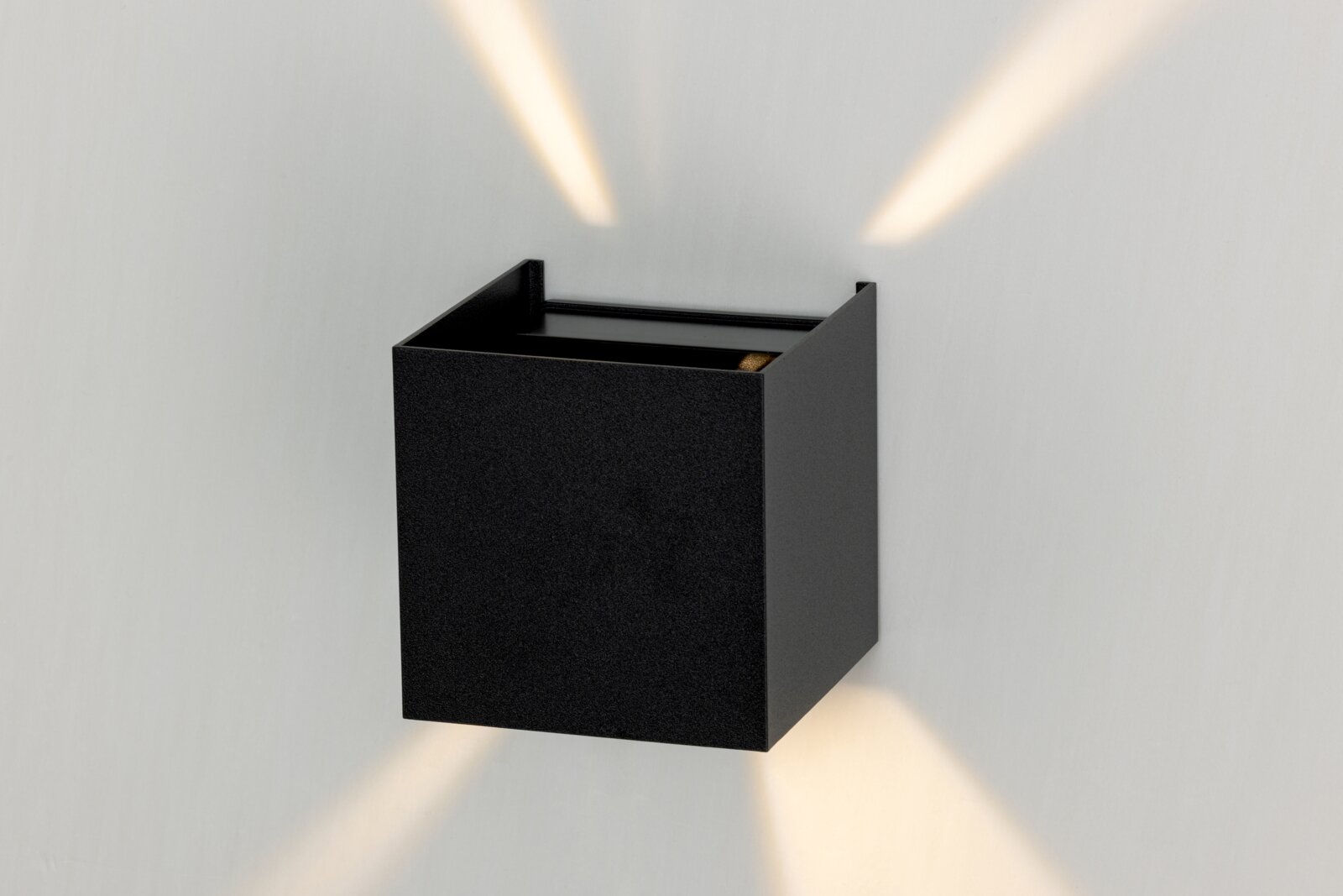 Schwarze LED-Wandleuchte in kubischer Form, die von der Seite betrachtet wird und Lichtstrahlen nach oben und unten abgibt.