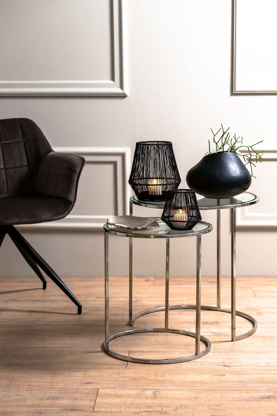 Zwei runde Beistelltische mit Glasplatten und Metallrahmen, dekoriert mit schwarzen Kerzenhaltern und einer Vase, seitliche Perspektive.