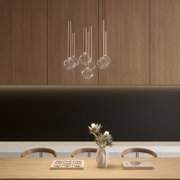 Moderne Pendelleuchte mit mehreren kupferfarbenen Röhren und klaren Glaskugeln über einem Esstisch in einem minimalistischen Interieur, frontale Ansicht