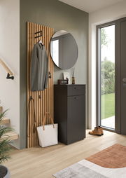 Runder Wandspiegel in einem modernen Flur, neben einer Garderobe mit Holzpaneelen und einem schwarzen Schrank, aus der Perspektive des Eingangsbereichs.