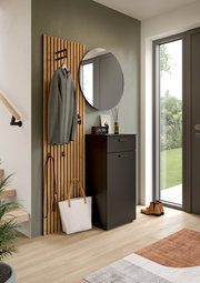Runder Wandspiegel in einem modernen Flur, neben einer Garderobe mit Holzpaneelen und einem schwarzen Schrank, aus der Perspektive des Eingangsbereichs.