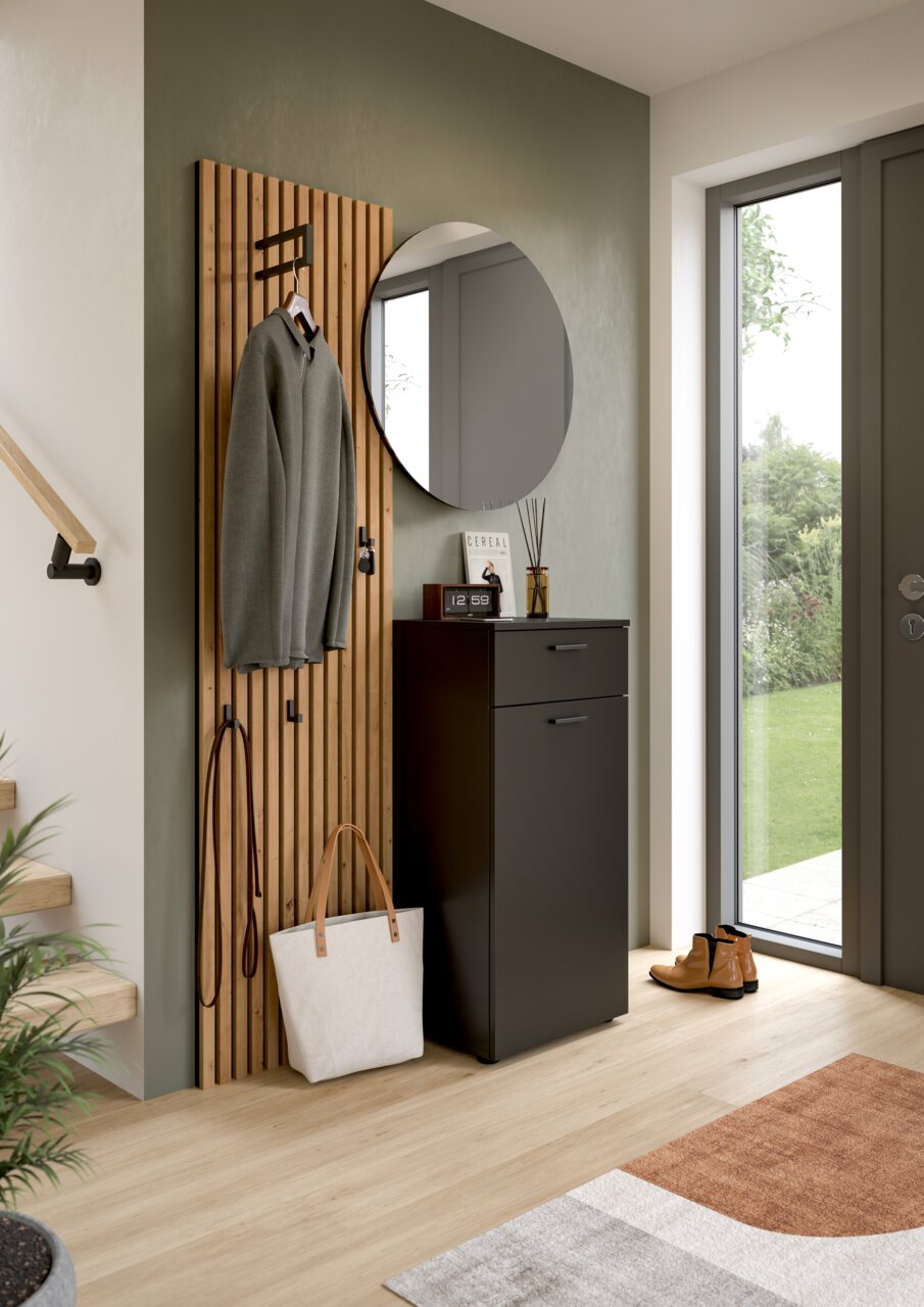 Runder Wandspiegel in einem modernen Flur, neben einer Garderobe mit Holzpaneelen und einem schwarzen Schrank, aus der Perspektive des Eingangsbereichs.