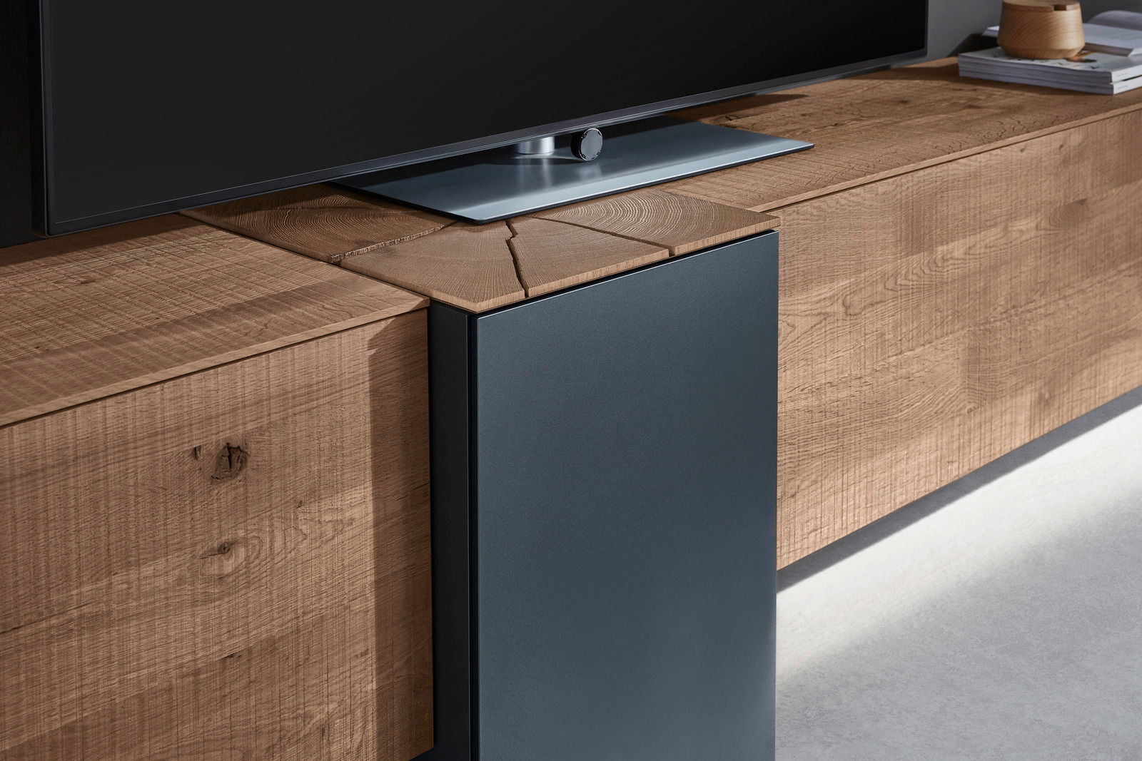 Nahaufnahme einer modernen Wandkombination aus Holz mit einer dunklen Metallverkleidung, auf der ein Fernseher steht. Perspektive von der Seite.
