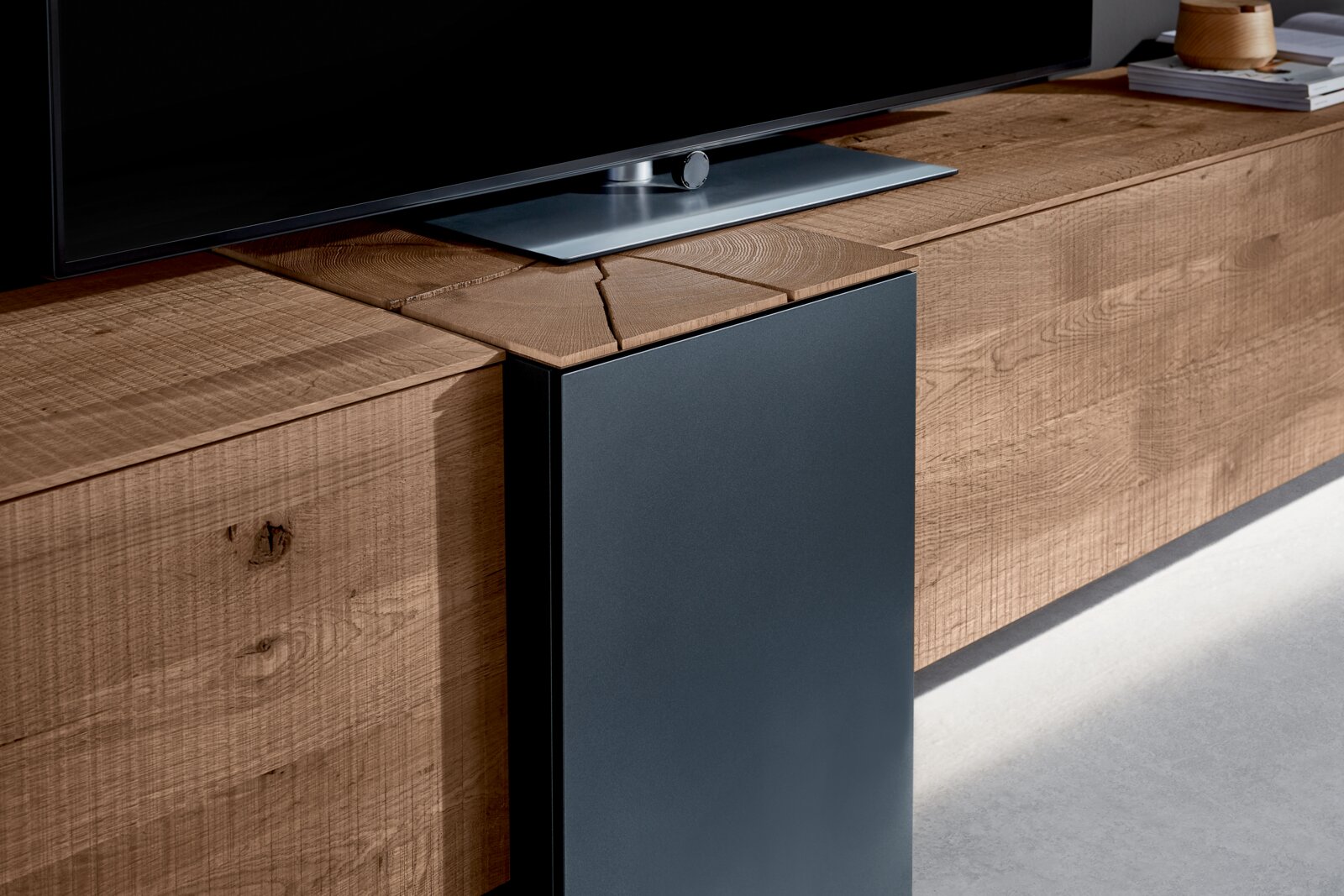 Close-up van een moderne wandcombinatie van hout met een donkere metalen bekleding, waarop een televisie staat. Zijaanzicht.
