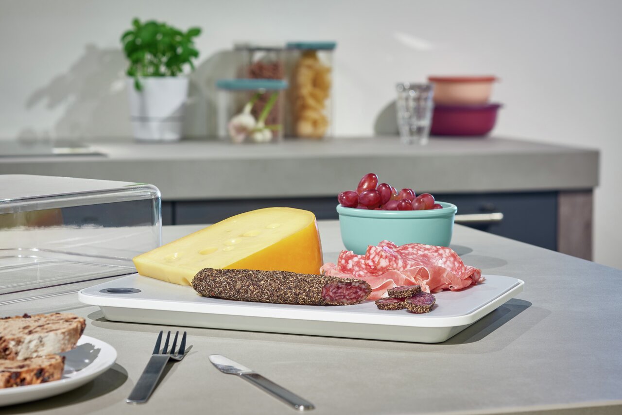 Ein Modula Starter-Set mit einer weißen Platte, darauf Käse, Wurst und Trauben, aus einer seitlichen Perspektive fotografiert.