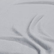 Nahaufnahme eines hellgrauen Spannbetttuchs mit weicher Textur und Falten, von oben betrachtet.