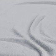 Nahaufnahme eines hellgrauen Spannbetttuchs mit weicher Textur und Falten, von oben betrachtet.