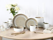 Kombiservice 16-tlg. Sand auf einem Tisch, bestehend aus Tellern, Schalen und Tassen in einem eleganten, sandfarbenen Design. Perspektive von vorne.