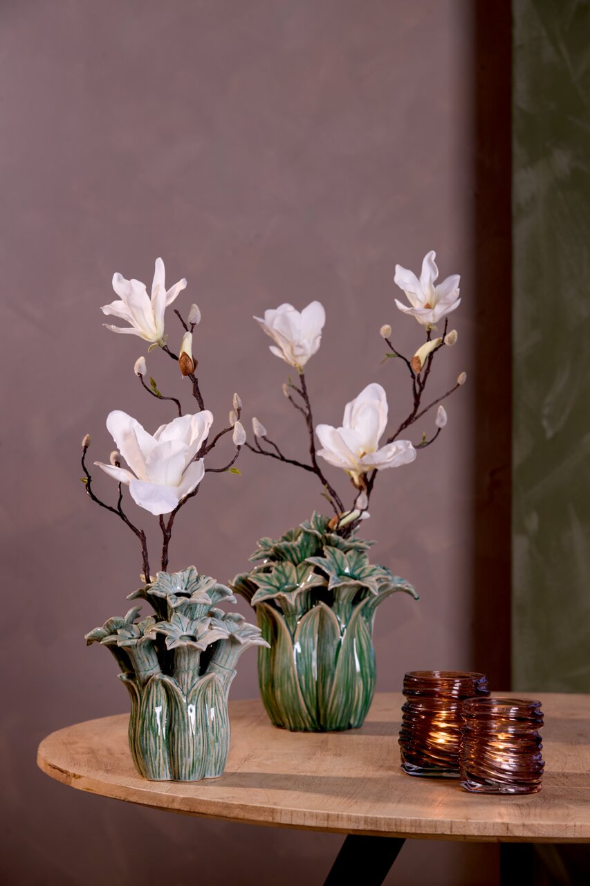 Zwei dekorative Teelichthalter aus braunem Glas auf einem Holztisch, im Hintergrund zwei Vasen mit weißen Blumen, seitliche Perspektive.