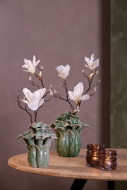 Zwei dekorative Teelichthalter aus braunem Glas auf einem Holztisch, im Hintergrund zwei Vasen mit weißen Blumen, seitliche Perspektive.