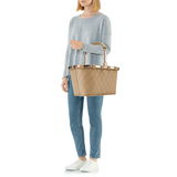 Frau in lässiger Kleidung hält eine beige, rautenförmig gesteppte Tragetasche mit Griffen, seitliche Perspektive