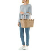 Frau in lässiger Kleidung hält eine beige, rautenförmig gesteppte Tragetasche mit Griffen, seitliche Perspektive