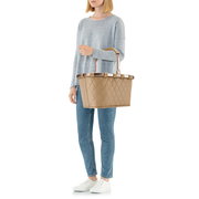 Frau in lässiger Kleidung hält eine beige, rautenförmig gesteppte Tragetasche mit Griffen, seitliche Perspektive