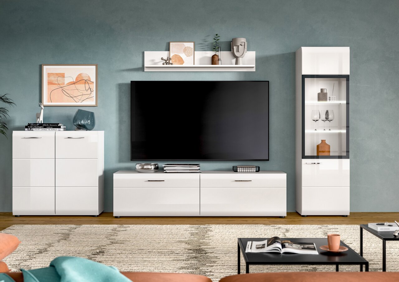 Modernes Wohnzimmer-Set in Weiß mit TV-Lowboard, Sideboard, Vitrine und Wandregal vor blaugrüner Wand, frontal aus Augenhöhe fotografiert