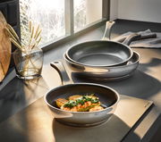 Pfannen-Set 3-tlg. in den Größen 20, 24 und 28 cm, auf einer Küchenarbeitsplatte präsentiert, mit einer Pfanne im Vordergrund, die ein Gericht enthält, seitliche Perspektive.