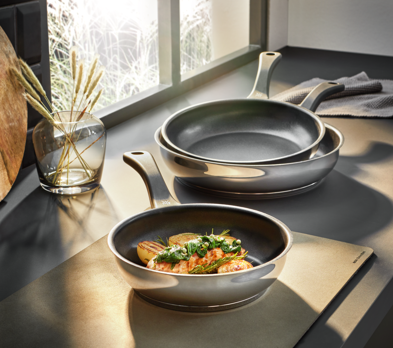 Pfannen-Set 3-tlg. in den Größen 20, 24 und 28 cm, auf einer Küchenarbeitsplatte präsentiert, mit einer Pfanne im Vordergrund, die ein Gericht enthält, seitliche Perspektive.