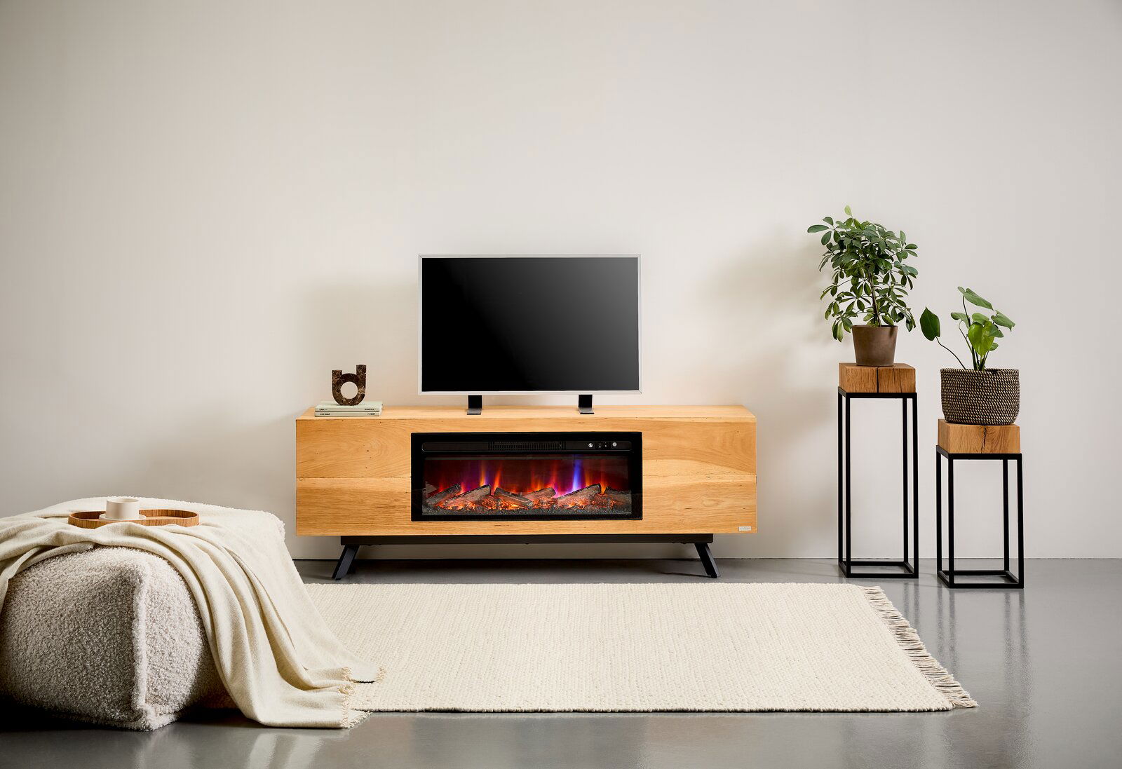Modernes TV-Lowboard aus hellem Holz mit integriertem Elektrokamin und Flammeneffekt, TV obenauf, frontal aus Augenhöhe im Wohnzimmer-Setting fotografiert.