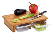 Schneidebrett aus Holz mit zwei Auffangschalen, darauf liegen ein Messer, eine Aubergine, eine rote Paprika und ein Lauch. Perspektive von schräg oben.