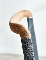 Nahaufnahme eines Freischwinger-Stuhls mit einem eleganten Holzgriff und einem mit Stoff bezogenen Gestell, seitliche Perspektive.