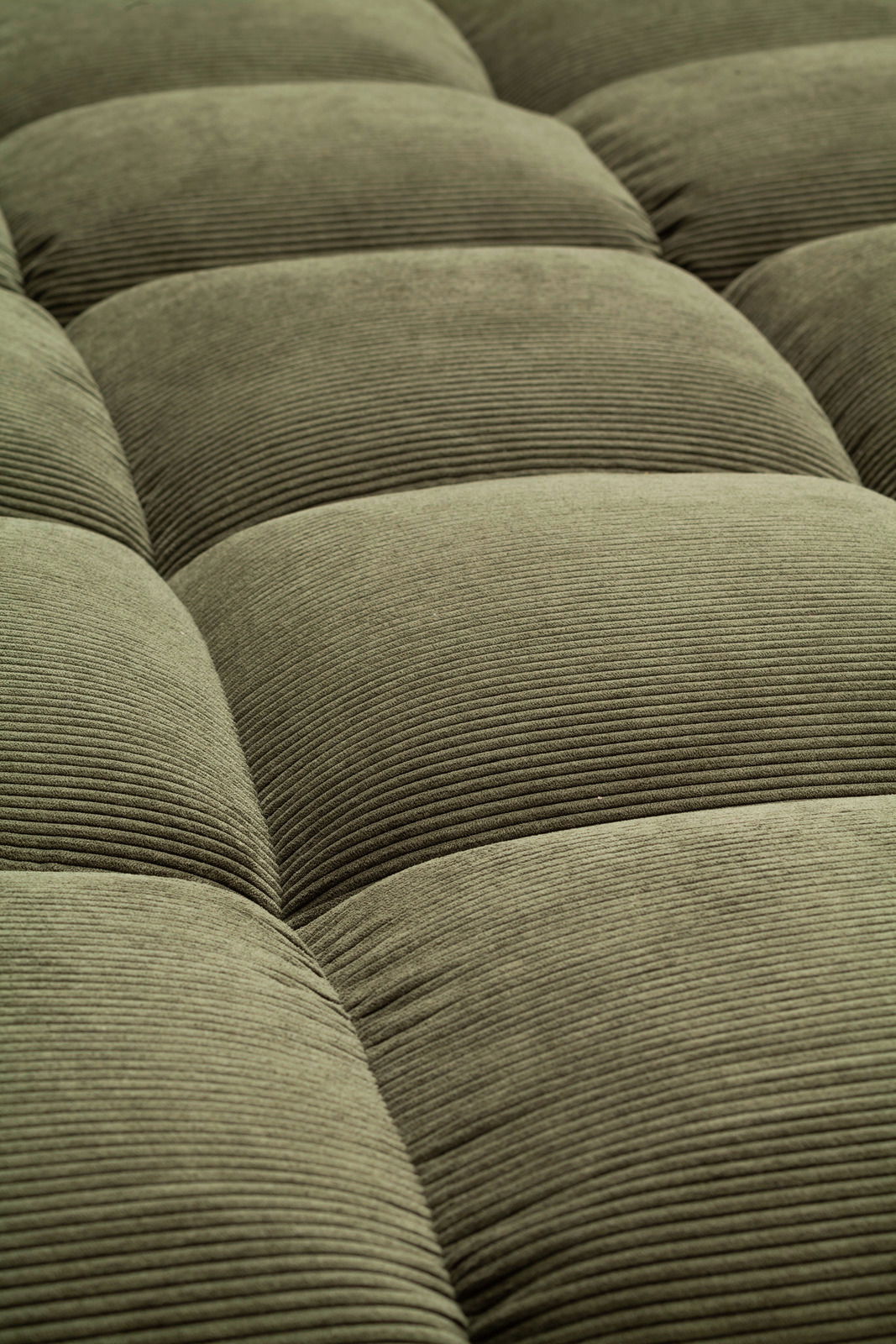 Nahaufnahme einer grünen, gesteppten Polsteroberfläche mit feiner Rillenstruktur, perspektivisch von oben betrachtet.