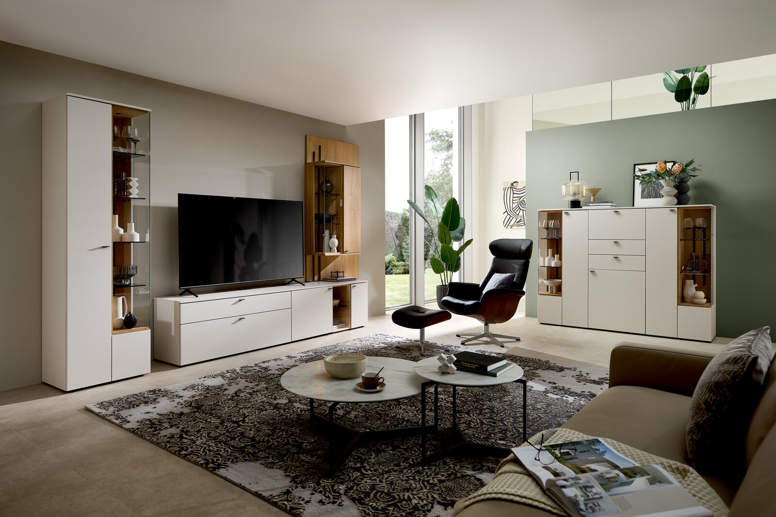 Modernes Wohnzimmer mit Highboard in Weiß, seitliche Perspektive. Das Highboard steht an einer grünen Wand, umgeben von stilvollen Möbeln und Dekorationen.