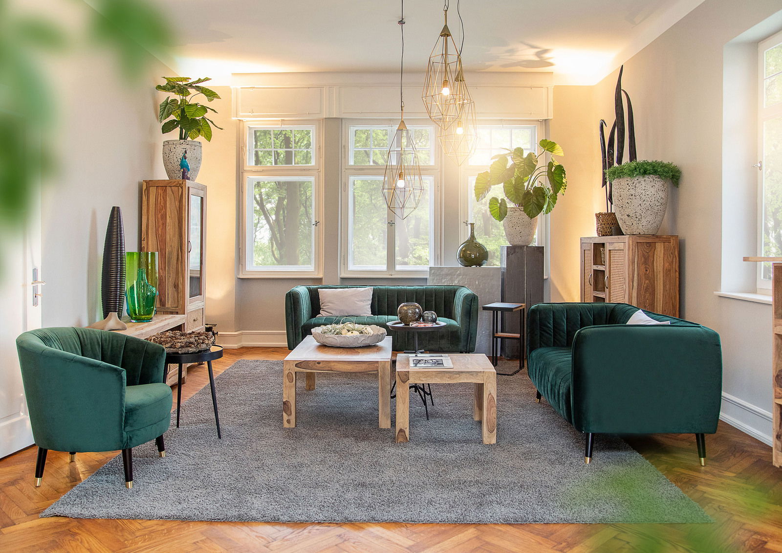 Wohnzimmer mit grünen Samtsofas, Holzcouchtisch und Pflanzen, seitliche Perspektive