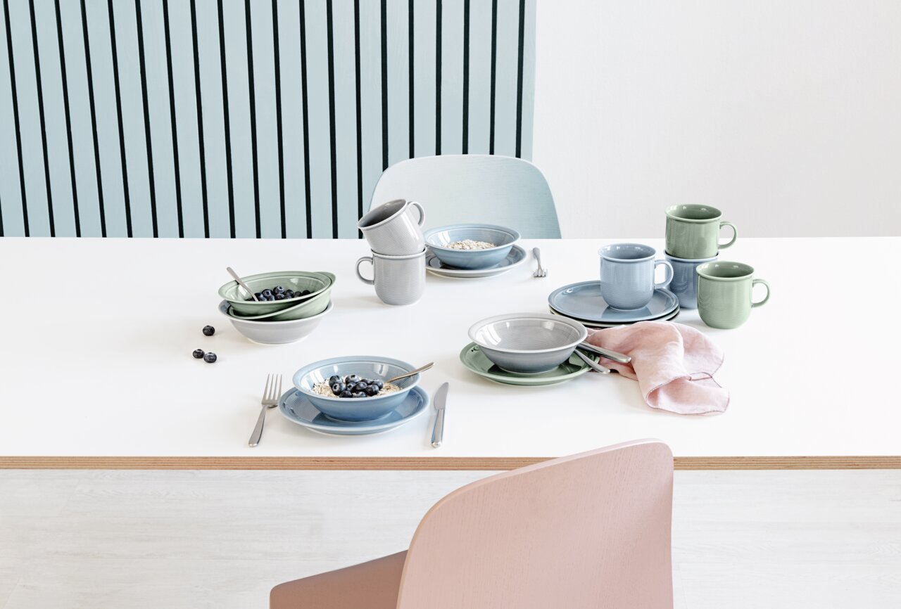 Ontbijtset van 18-delig in zachte pasteltinten, bestaande uit kopjes, borden en schalen, van bovenaf gefotografeerd op een witte tafel.