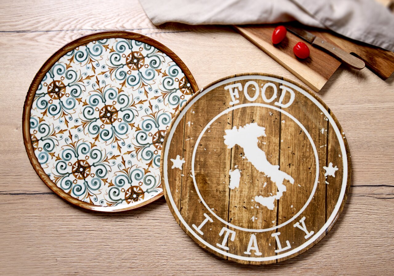 Zwei Pizzateller aus der Vogelperspektive: Einer mit floralem Muster in Grün und Braun, der andere mit rustikalem Holzdesign und Italien-Motiv.