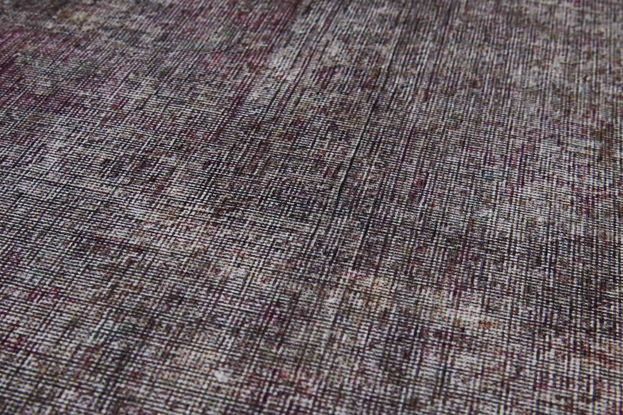 Nahaufnahme eines Teppichs mit einem komplexen, mehrfarbigen Muster in gedeckten Tönen, aus einer schrägen Perspektive aufgenommen.