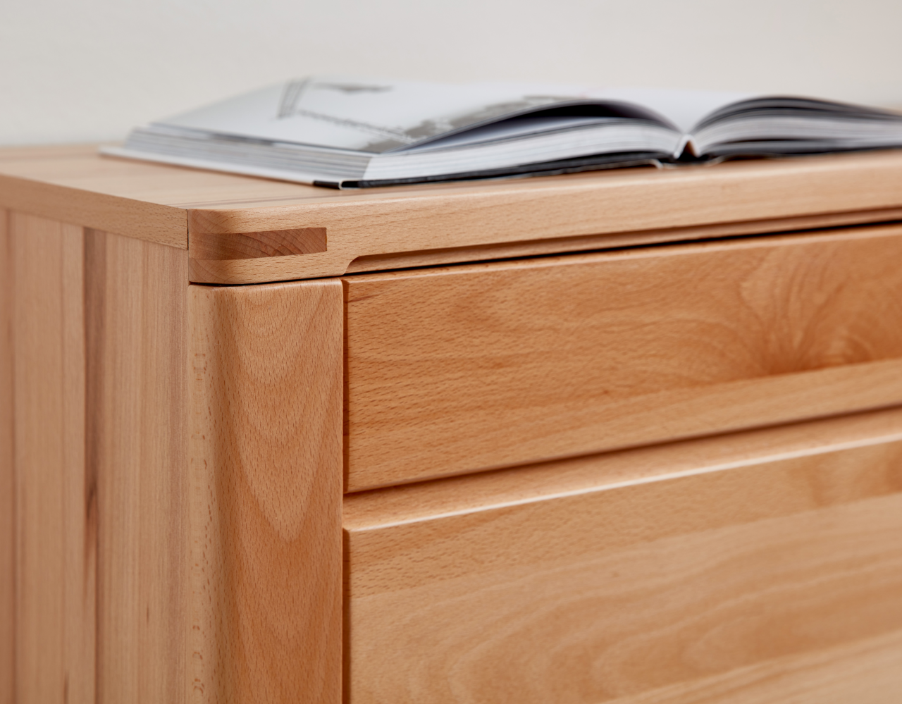 Nahaufnahme eines hölzernen Sideboards mit geöffneter Schublade und einem Buch darauf, aus seitlicher Perspektive.