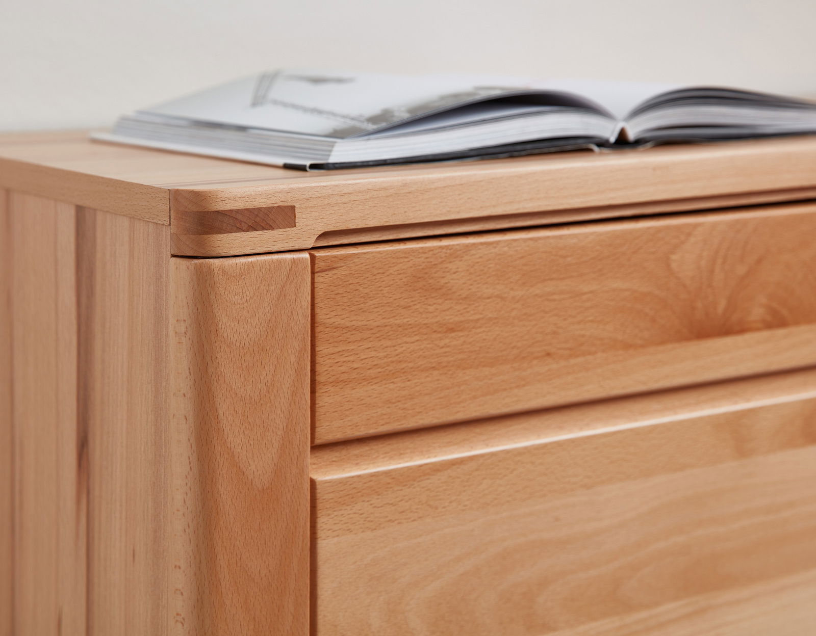 Nahaufnahme eines hölzernen Sideboards mit geöffneter Schublade und einem Buch darauf, aus seitlicher Perspektive.