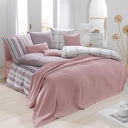 Een gezellig slaapkamerbeeld met een roze sprei op het bed, omringd door sierkussens in verschillende patronen en kleuren.