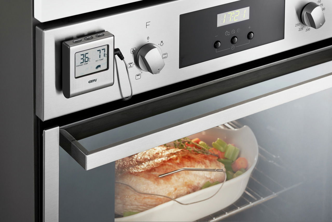 Digitales Bratenthermometer an einem Ofen, das die Temperatur eines Bratens im Inneren misst, seitliche Perspektive