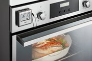 Digitales Bratenthermometer an einem Ofen, das die Temperatur eines Bratens im Inneren misst, seitliche Perspektive