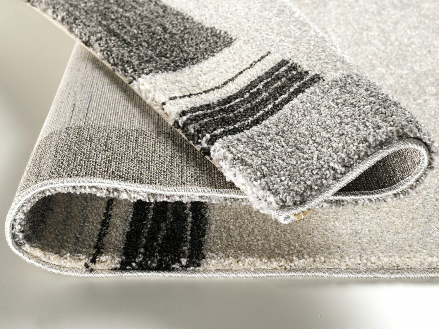 Nahaufnahme eines gefalteten Teppichs mit grauen und schwarzen Streifen, Perspektive von der Seite