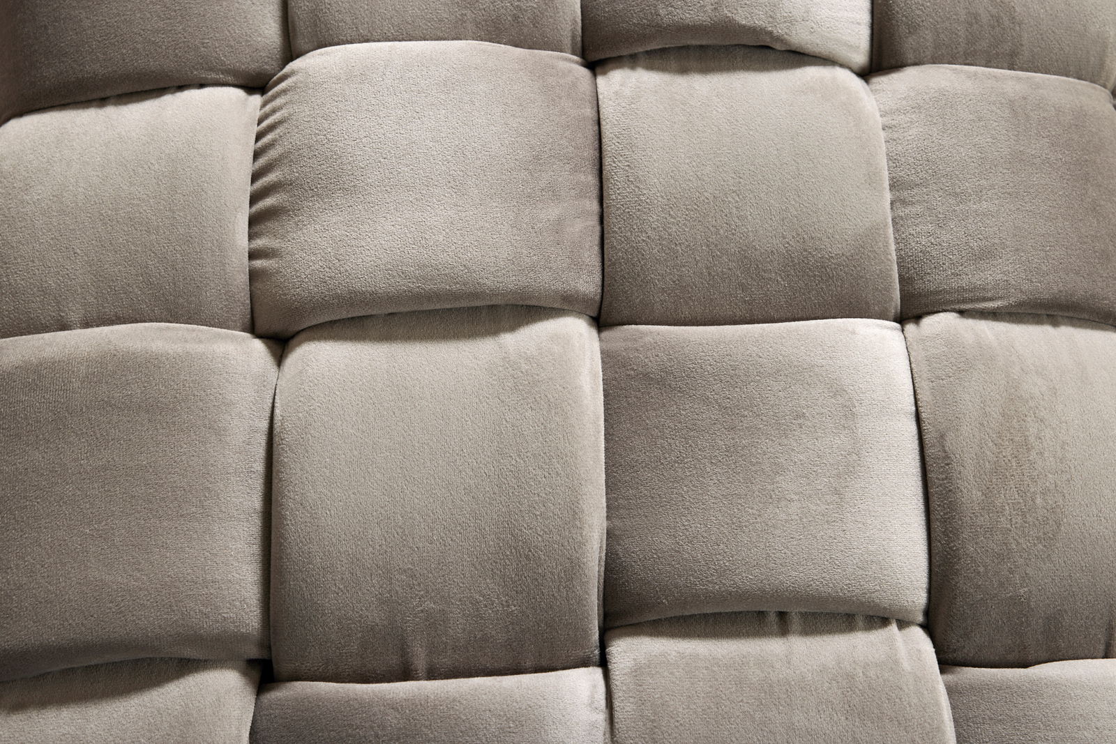 Nahaufnahme eines gepolsterten Hockers mit weichem, grauem Stoff in einem quadratischen Muster.