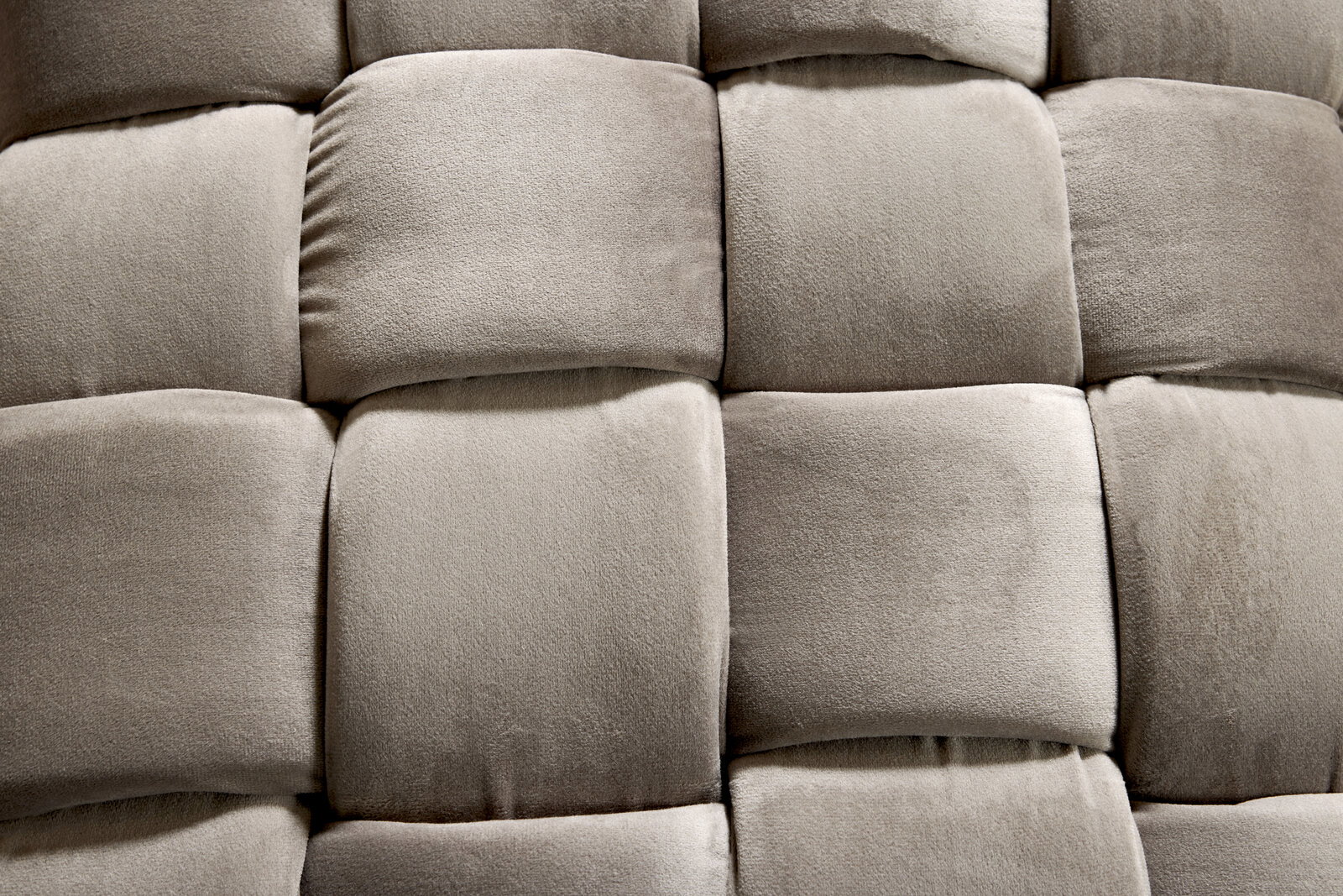 Nahaufnahme eines gepolsterten Hockers mit weichem, grauem Stoff in einem quadratischen Muster.