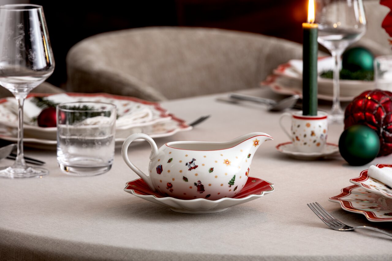Weihnachtlich dekorierte Sauciere mit Unterteil auf einem festlich gedeckten Tisch, seitliche Perspektive