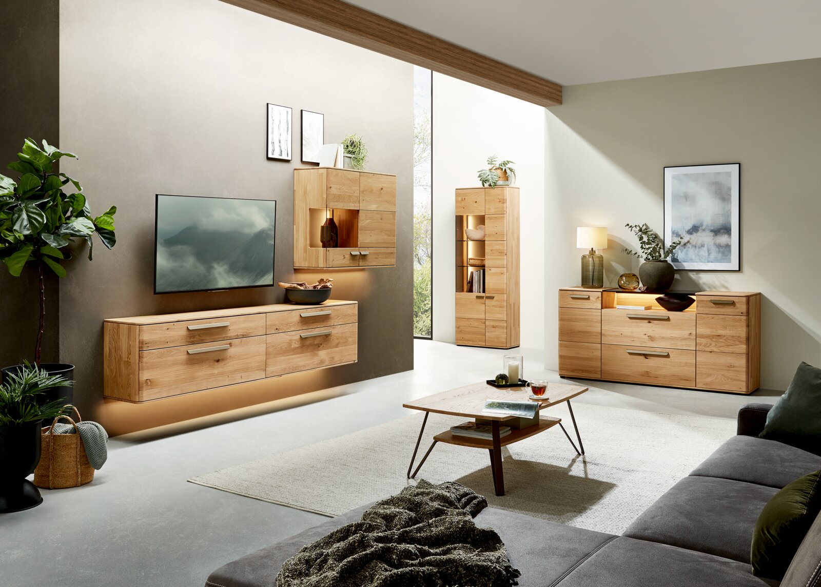 Valnatura Couchtisch LERIDA Modernes Wohnzimmer mit hellen Massivholz-Möbeln: schwebendes TV-Lowboard, Hängeelement mit Beleuchtung, Vitrine und Sideboard mit Griffen; Frontansicht aus leicht schräger Perspektive.