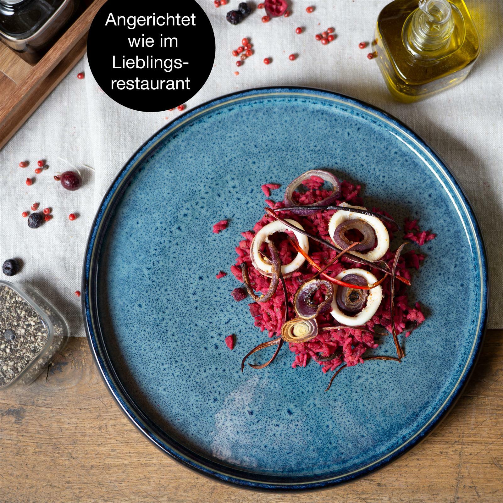 Blauer Teller mit kunstvoll angerichtetem Essen aus der Vogelperspektive, umgeben von Gewürzen und Ölflasche.