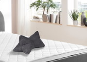 Grauer Leseknochen auf einem weißen Bett, seitliche Perspektive, mit Pflanzen und Büchern im Hintergrund.