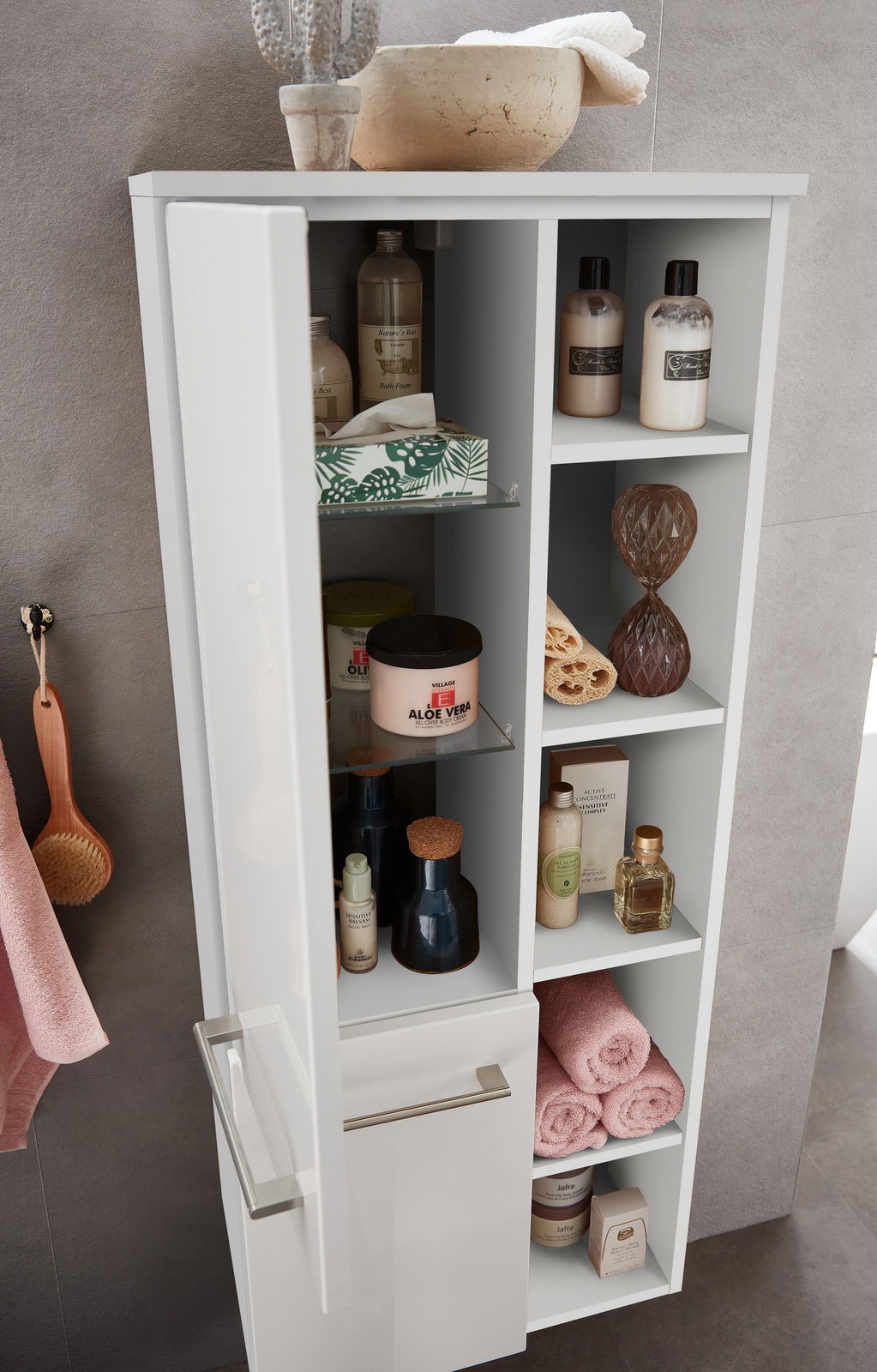 Moderner Midischrank mit geöffneter Tür, gefüllt mit Pflegeprodukten und Handtüchern, aus der Perspektive von schräg oben fotografiert.