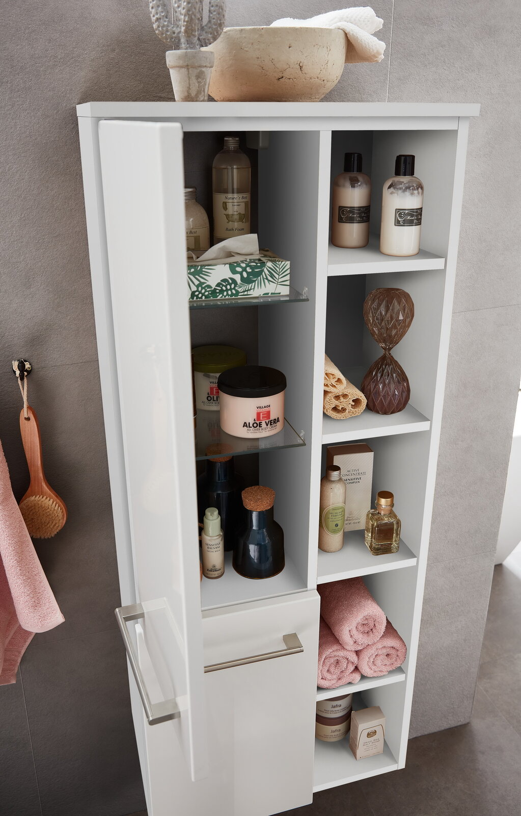 Moderner Midischrank mit geöffneter Tür, gefüllt mit Pflegeprodukten und Handtüchern, aus der Perspektive von schräg oben fotografiert.