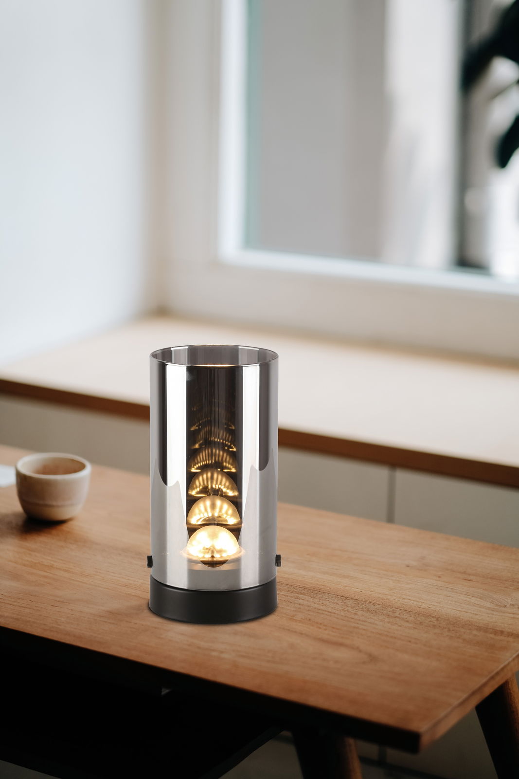 Moderne LED-Tischleuchte in zylindrischer Form auf einem Holztisch, seitliche Perspektive