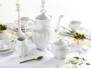 Weißes Porzellan-Kaffeeservice mit Kaffeekanne, Zuckerdose und Milchkännchen auf gedecktem Tisch, leicht von vorne in Augenhöhe fotografiert.