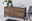 Holz-Sideboard mit drei Schubladen und zwei Türen, dekoriert mit Vasen und Pflanzen, aus seitlicher Perspektive fotografiert.