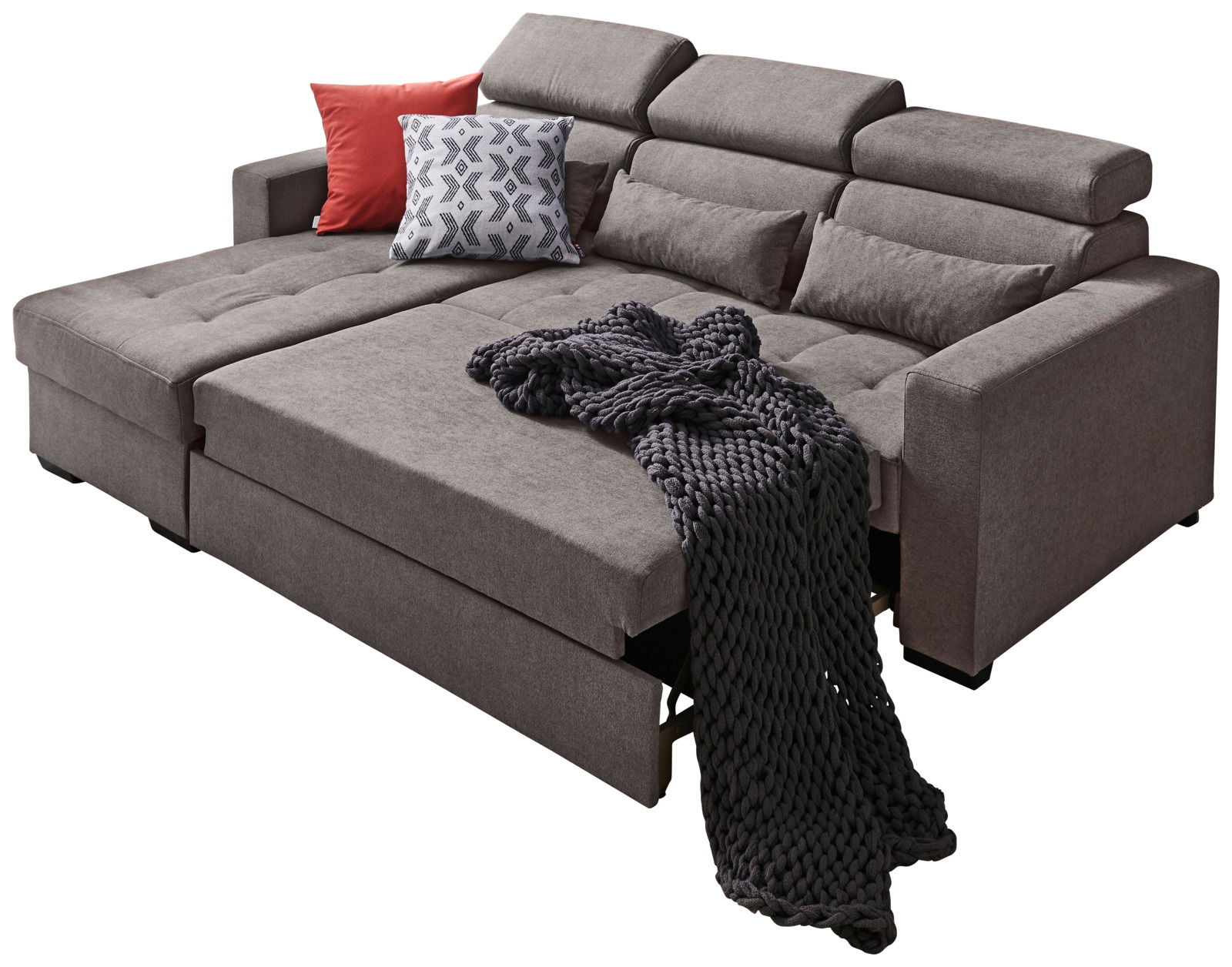Großes, modernes Ecksofa in Grau mit verstellbaren Kopfstützen, dekoriert mit roten und gemusterten Kissen sowie einer dunklen Strickdecke, Perspektive von vorne links.