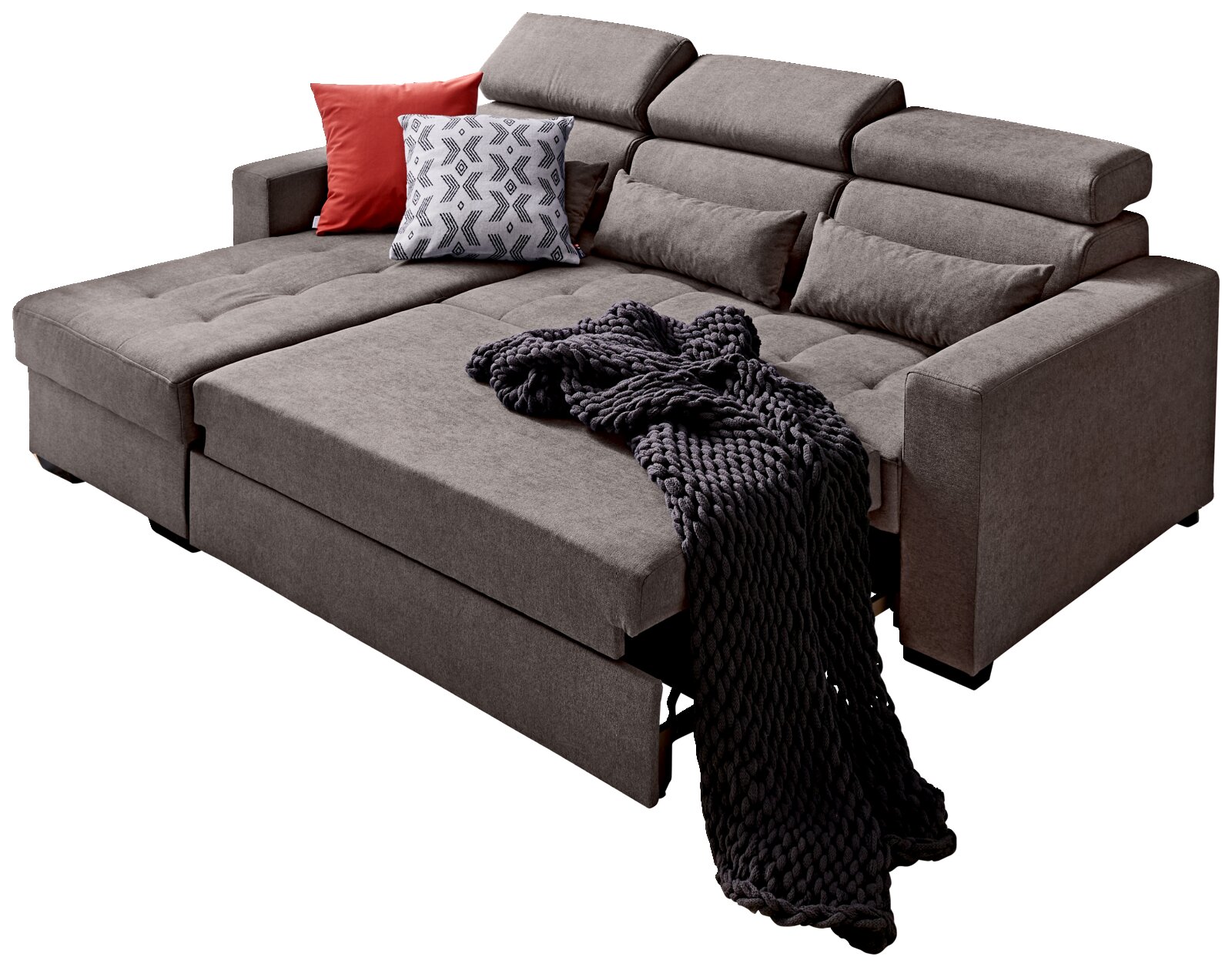 Ecksofa MONSON Großes, modernes Ecksofa in Grau mit verstellbaren Kopfstützen, dekoriert mit roten und gemusterten Kissen sowie einer dunklen Strickdecke, Perspektive von vorne links.
